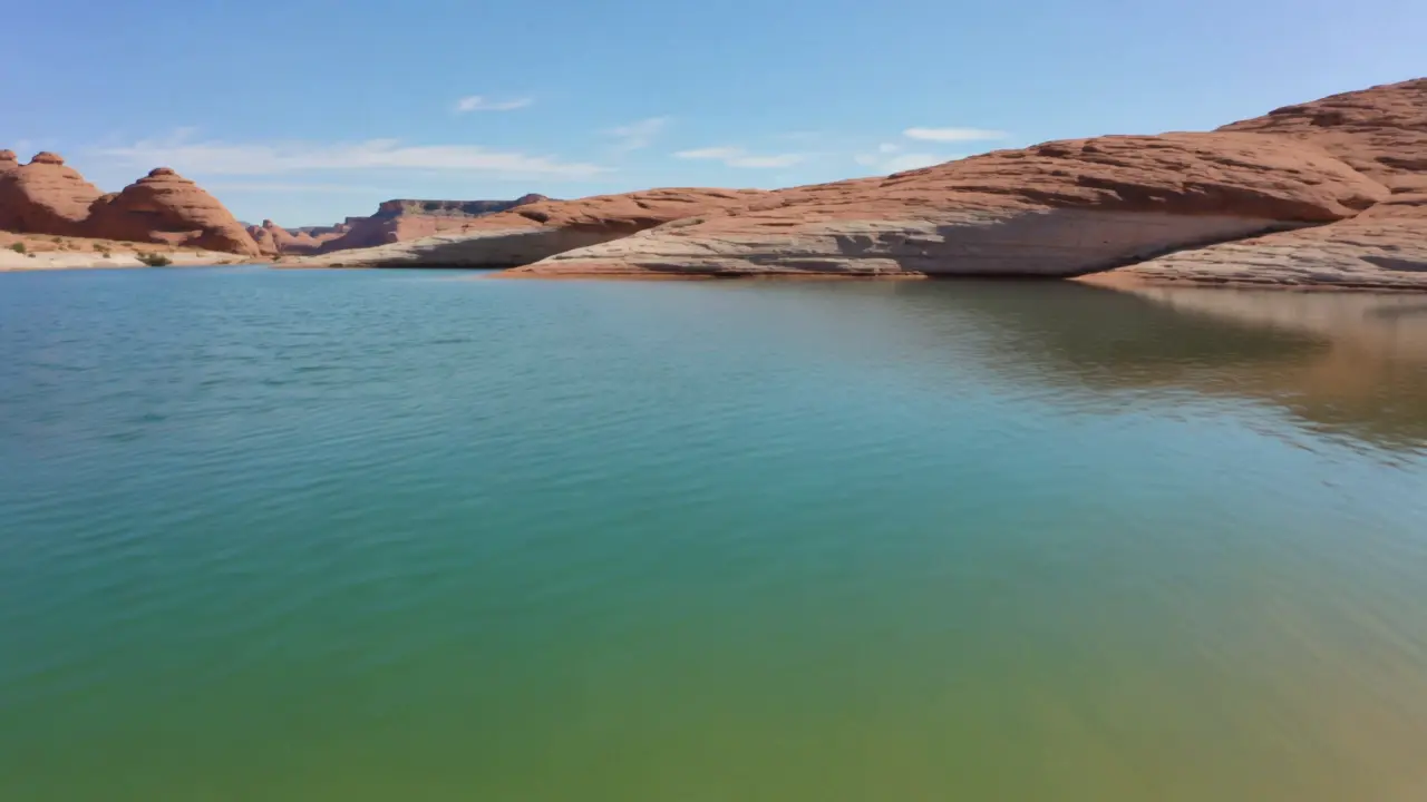 A turquoise desert reservoir with red sandstone shoreline and sand dunes